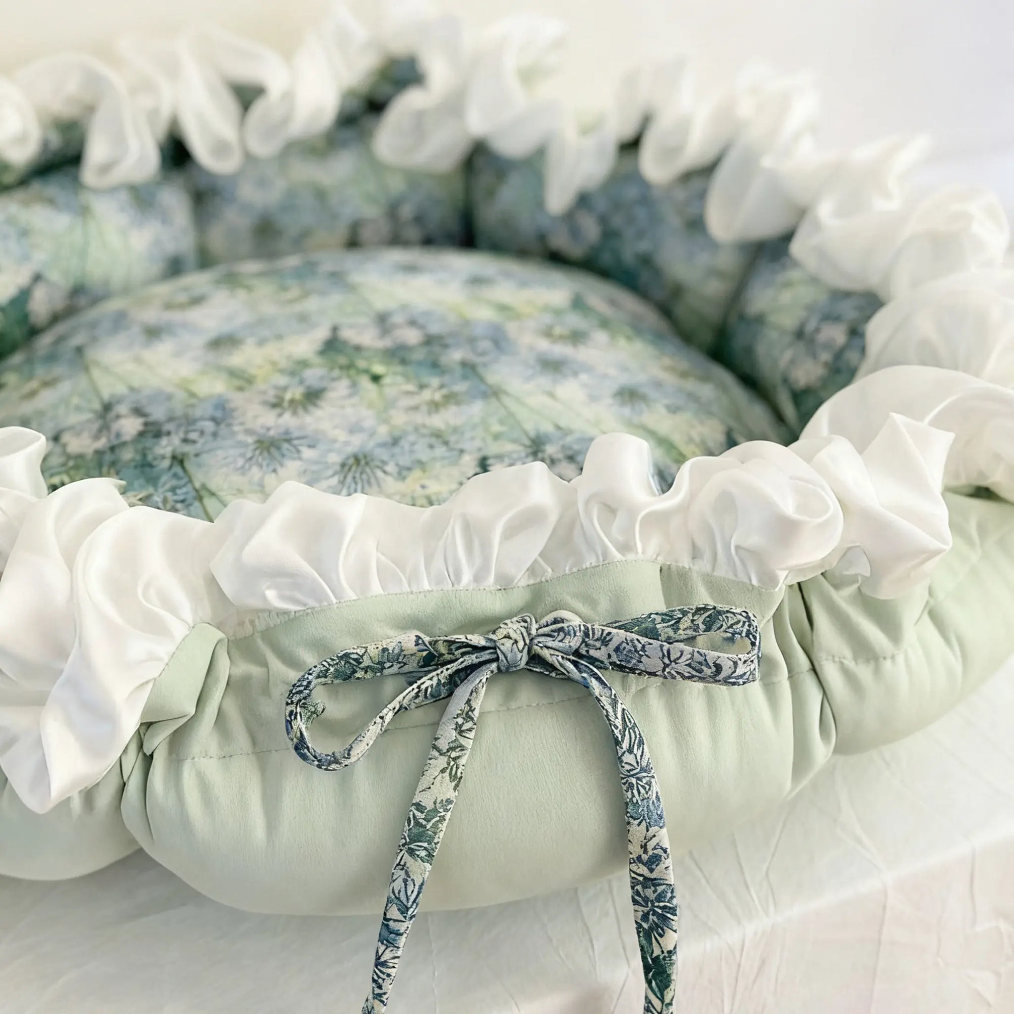 Floral pet bed with white ruffles and a ribbon tie, on a light background，Close-up of cotton fabric and rich oil painting style garden motif on cat bed