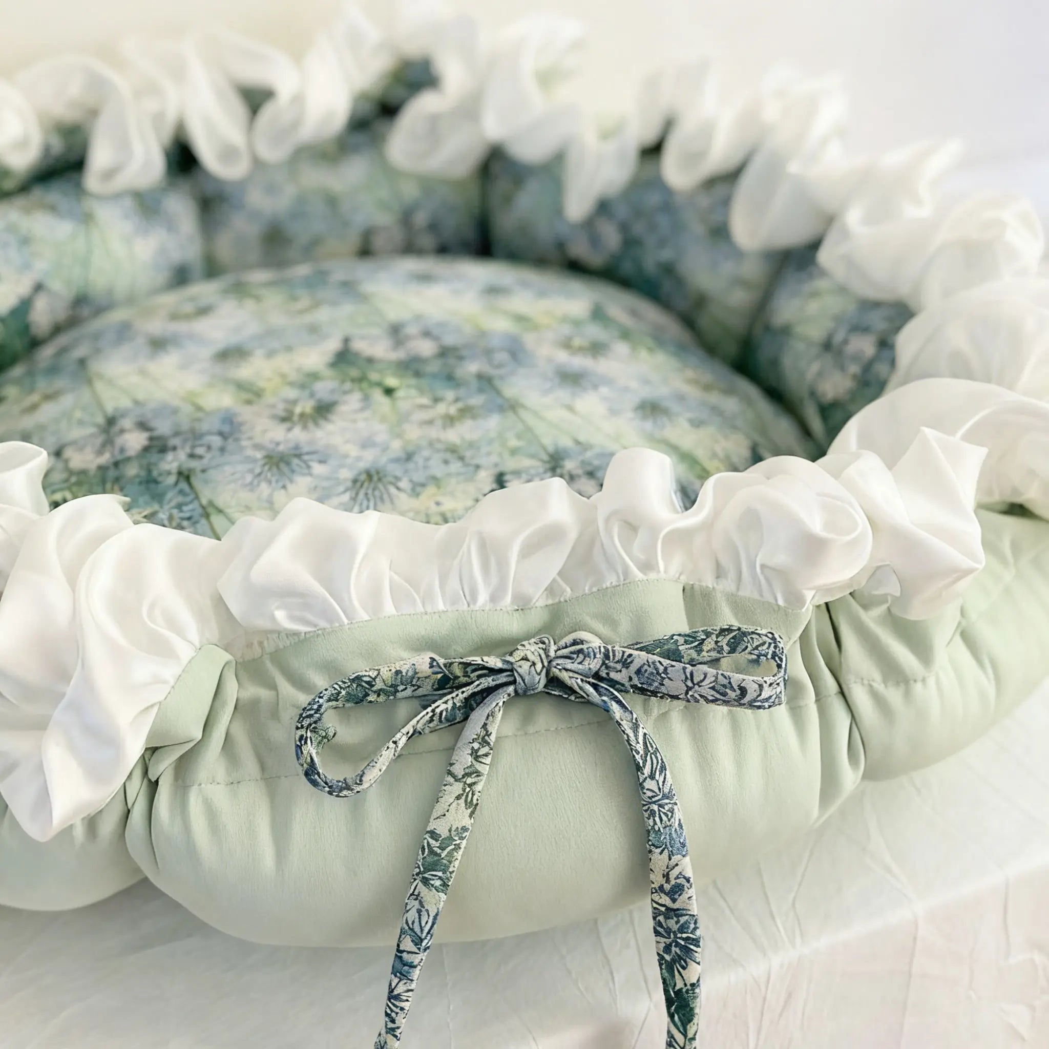 Floral pet bed with white ruffles and a ribbon tie, on a light background，Close-up of cotton fabric and rich oil painting style garden motif on cat bed
